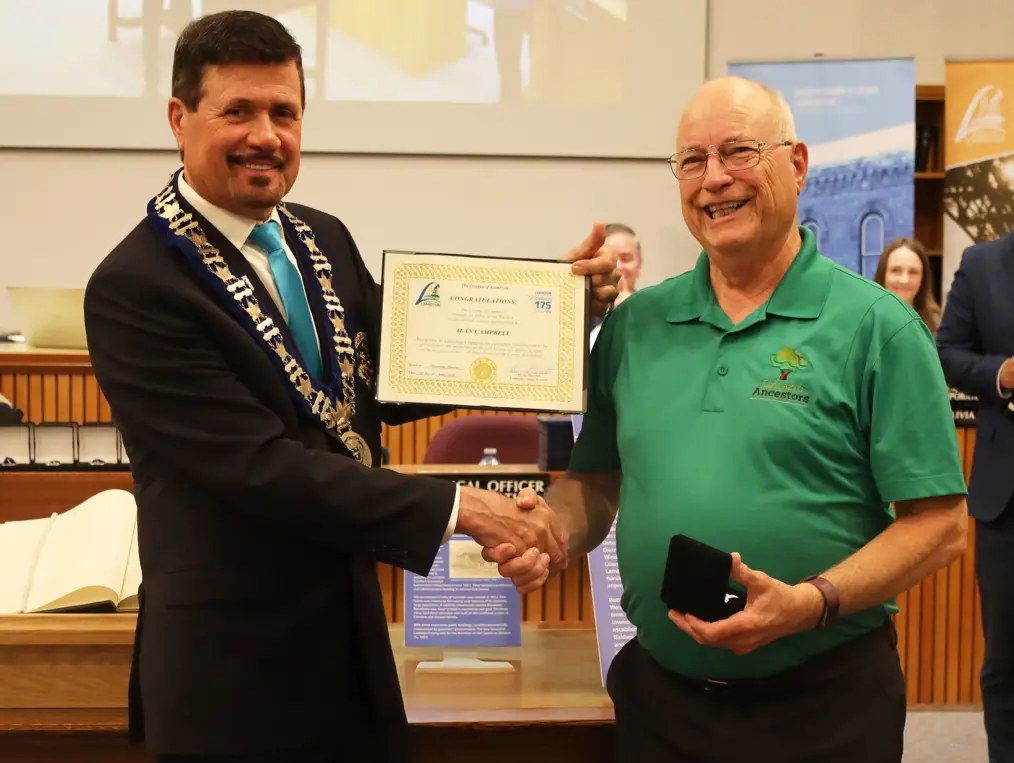 Photo of a man in collared shirt accepting certificate from another man with brown hair.