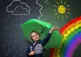 A boy in front of a chalkboard with different weather events drawn on it: rainbow, raining, sunny, etc.