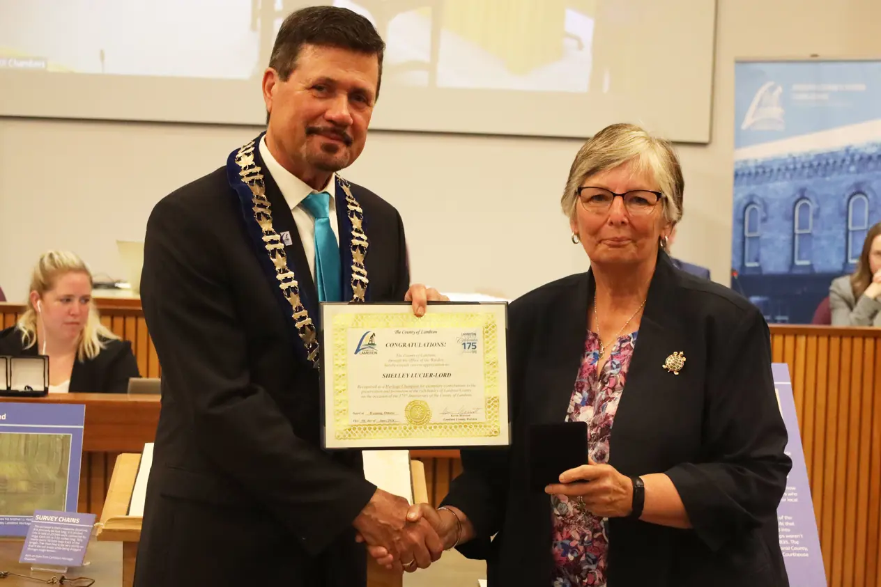 photo of a white woman in a suit accepting an award from a man in a suit.