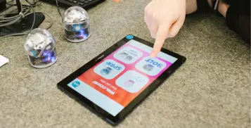 Finger touching screen of tablet on a table. 