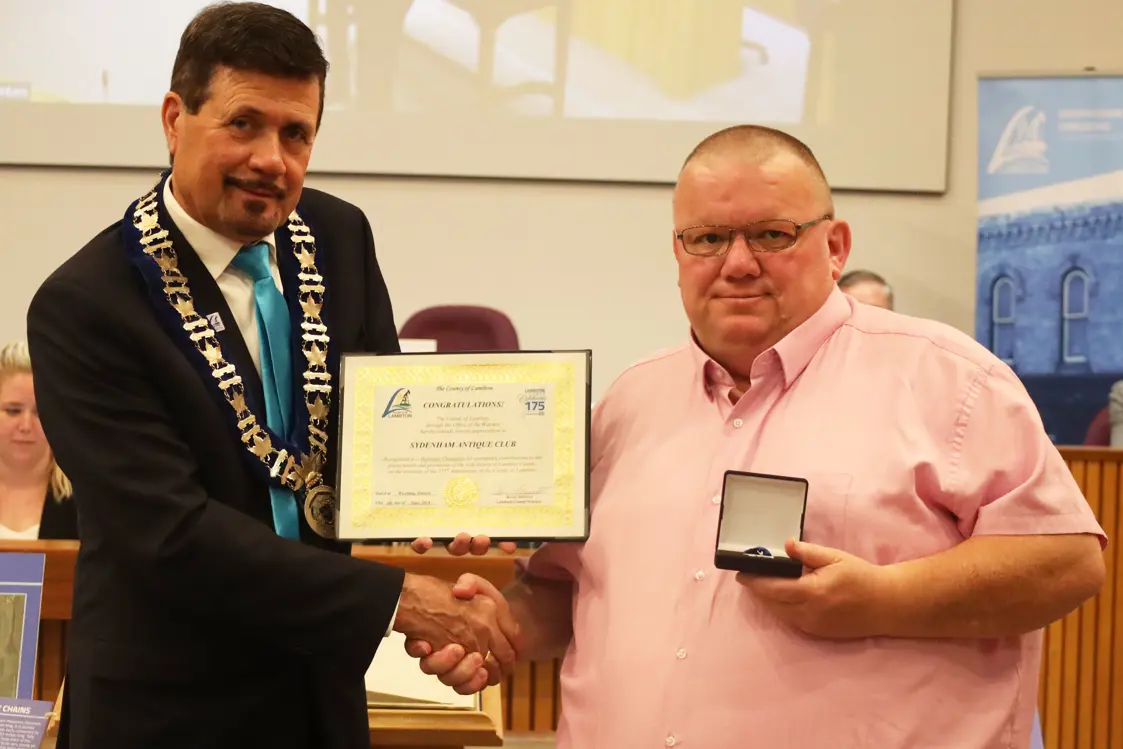 Photo of a man in collared shirt accepting certificate from another man with brown hair.