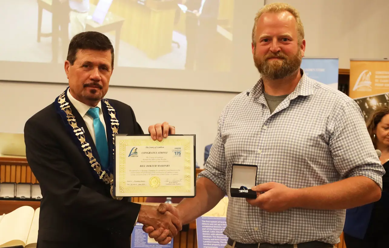 Photo of a man in collared shirt accepting certificate from another man with brown hair.