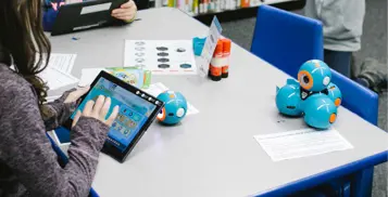 Blue robot sitting on table with tablet. 