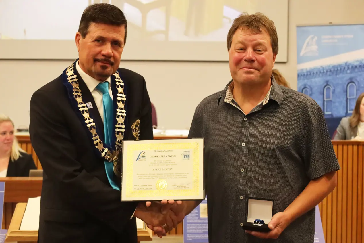 Photo of a man in collared shirt accepting certificate from another man with brown hair.