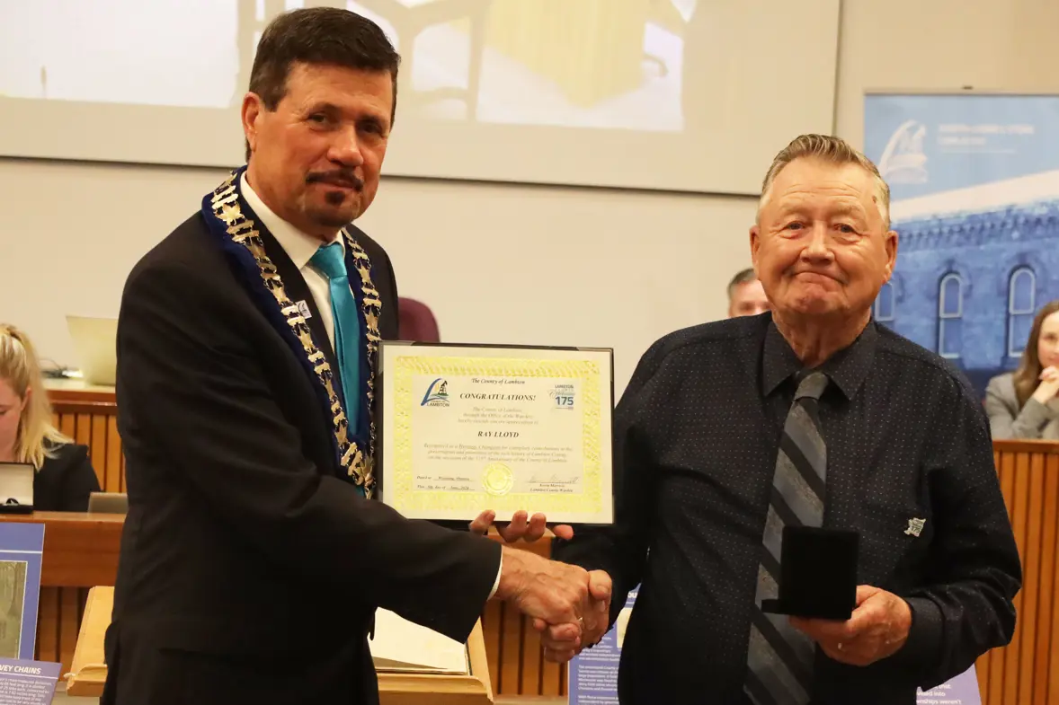 Photo of a man in a shirt and tie accepting an award from a man in a dark suit.