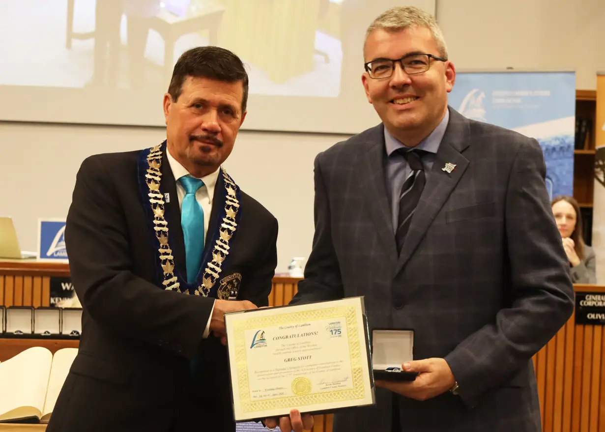 Photo of a man in a suit accepting certificate from another man with brown hair.