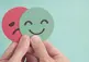 hands holding a red circle with an angry face and a teal circle with a happy face